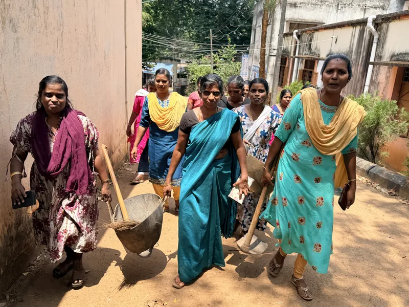 Women carrying cleaning tools and a wheelbarrow during the cleaning drive